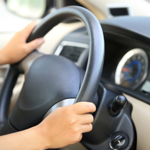 Two hands grip the steering wheel of a car