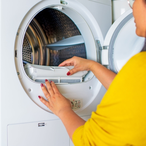 Woman in yellow sweater cleans a home clothes dryer vent