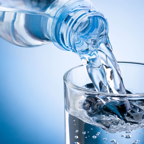 Pouring water from bottle into glass on blue background
