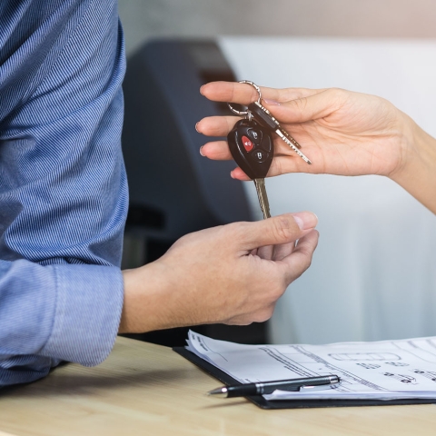 Close up view hands of agent giving car key to client renting a vehicle in rental office