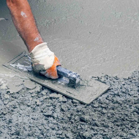 A hand wearing a glove smoothing out rough wet concrete at a work site