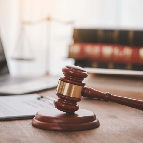 A laptop on a desk with paperwork, a gavel, and a stack of law books