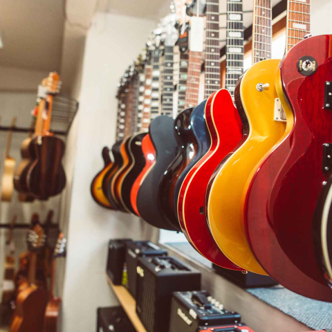 Row of colorful guitars hanging on display in a music store, with amplifiers and additional guitars visible in the background.