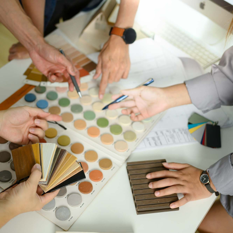 Overhead view of a group collaborating around a table, comparing color swatches, material samples, and design palettes while discussing interior design options