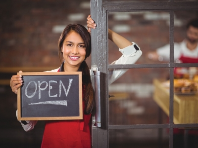 Worker standing in doorway holding Open sign