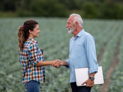A woman and a man shake hands in a farm field