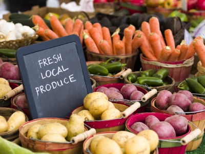 Fresh Local Produce sign at a farmer's market surrounded by potatoes, carrots, and other vegetables