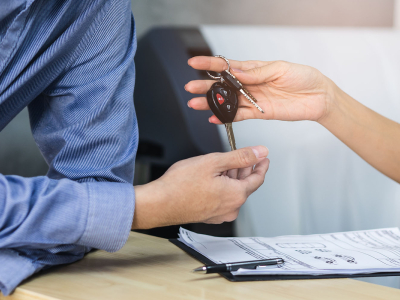 Close up view hands of agent giving car key to client renting a vehicle in rental office