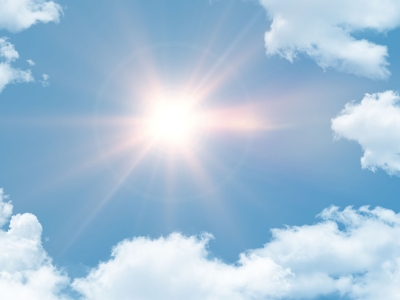 A bright hot sun shining in a cloudy blue sky
