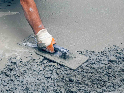 A hand wearing a glove smoothing out rough wet concrete at a work site