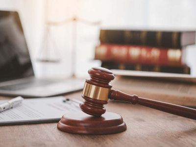 A laptop on a desk with paperwork, a gavel, and a stack of law books