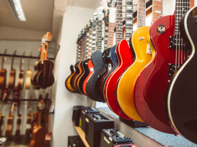 Row of colorful guitars hanging on display in a music store, with amplifiers and additional guitars visible in the background.