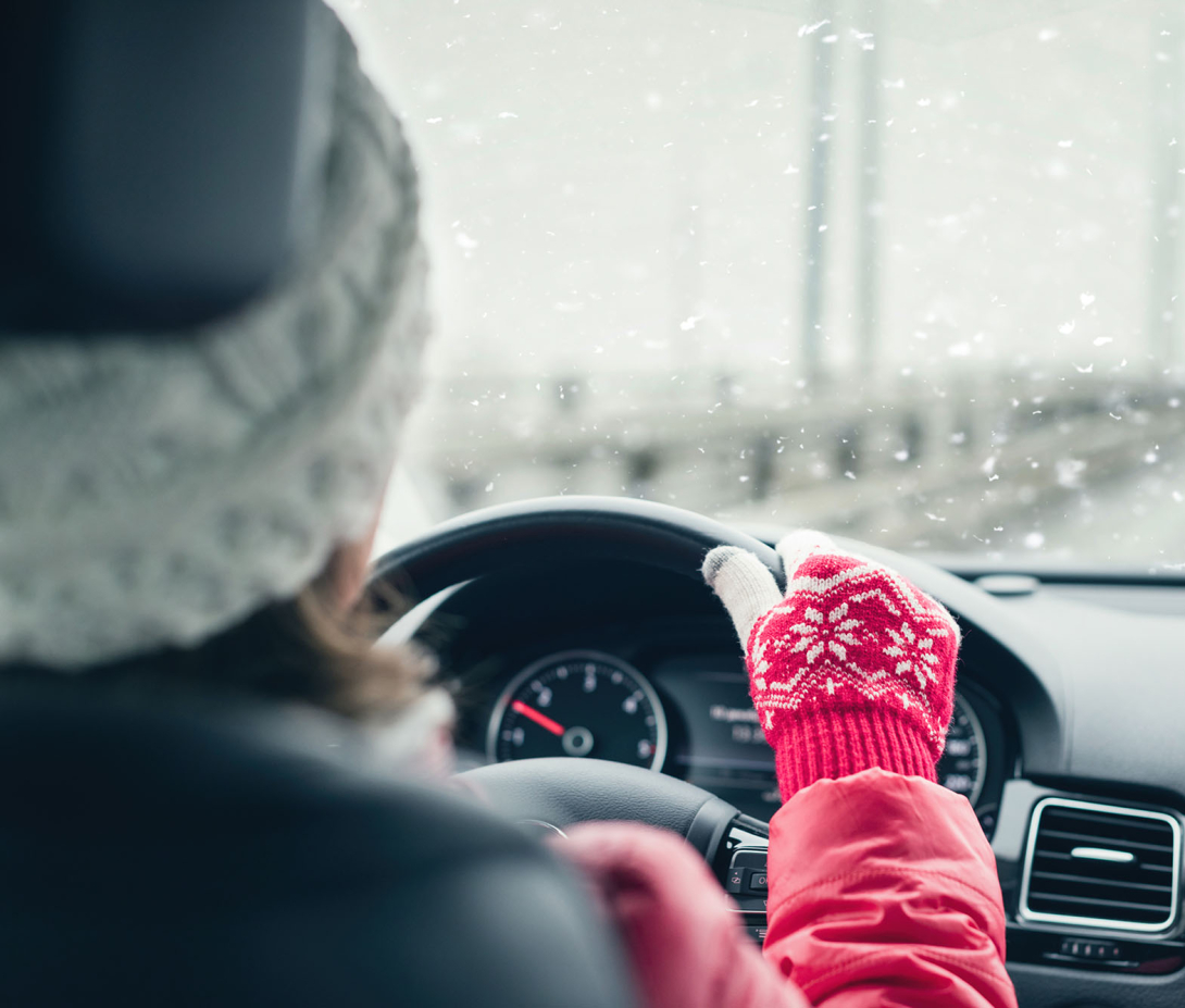 Woman in red jacket, hat, and gloves driving on highway during winter snowfall