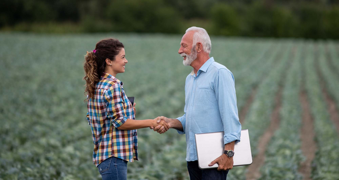 A woman and a man shake hands in a farm field