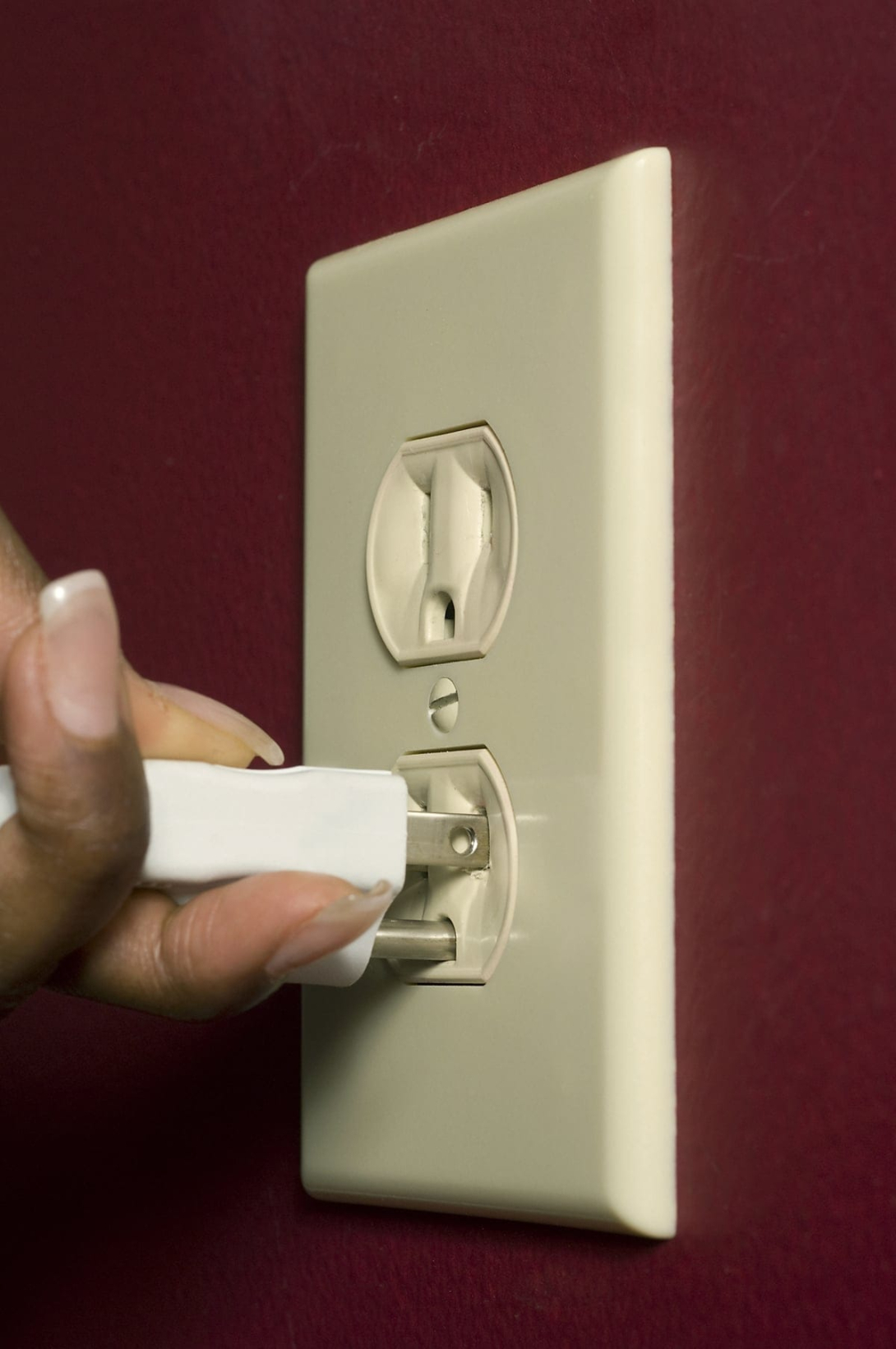 A hand plugging in an electrical cord into a wall outlet