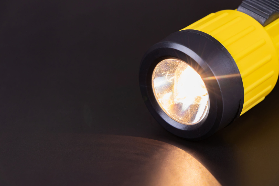 A lit yellow flashlight against a dark background