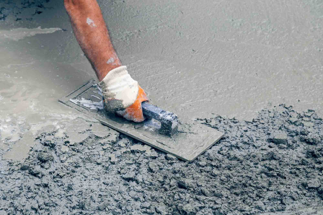 A hand wearing a glove smoothing out rough wet concrete at a work site