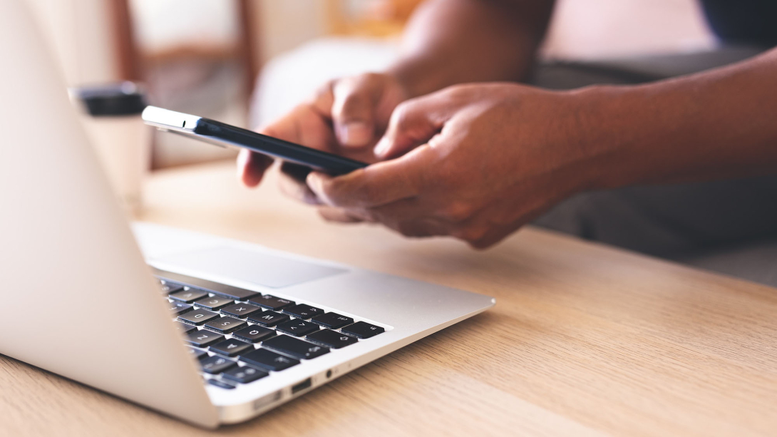 Hands on a cellphone over a laptop