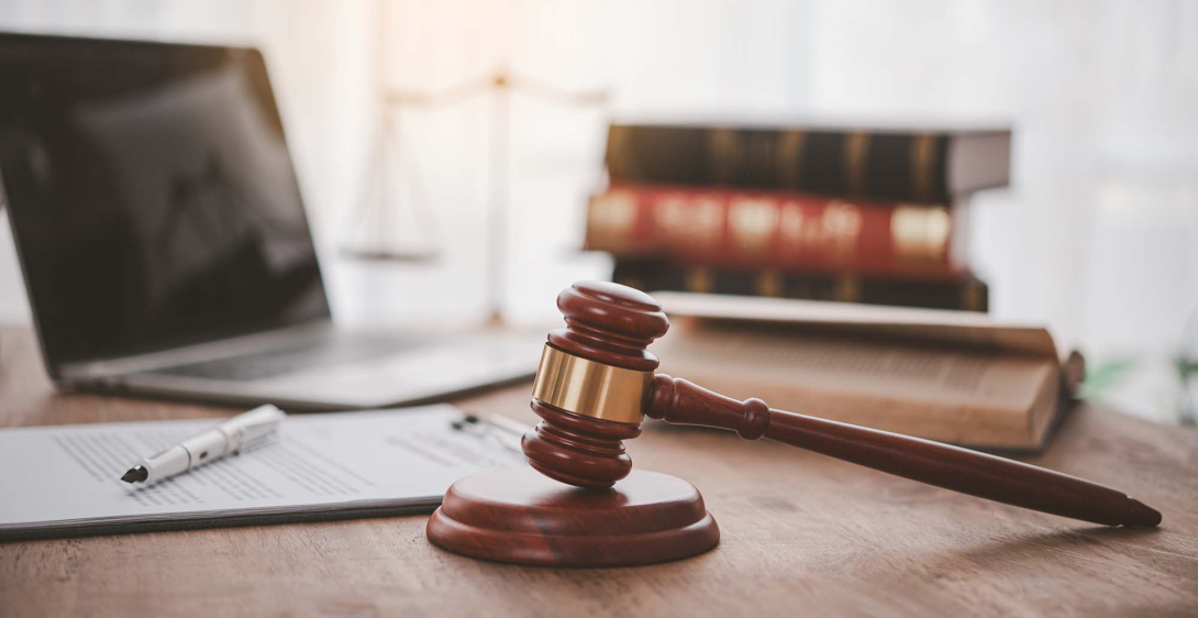 A laptop on a desk with paperwork, a gavel, and a stack of law books