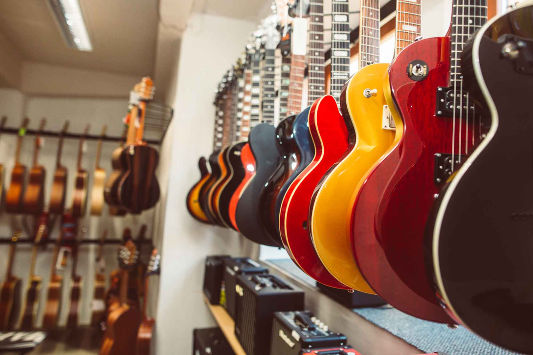 Row of colorful guitars hanging on display in a music store, with amplifiers and additional guitars visible in the background.
