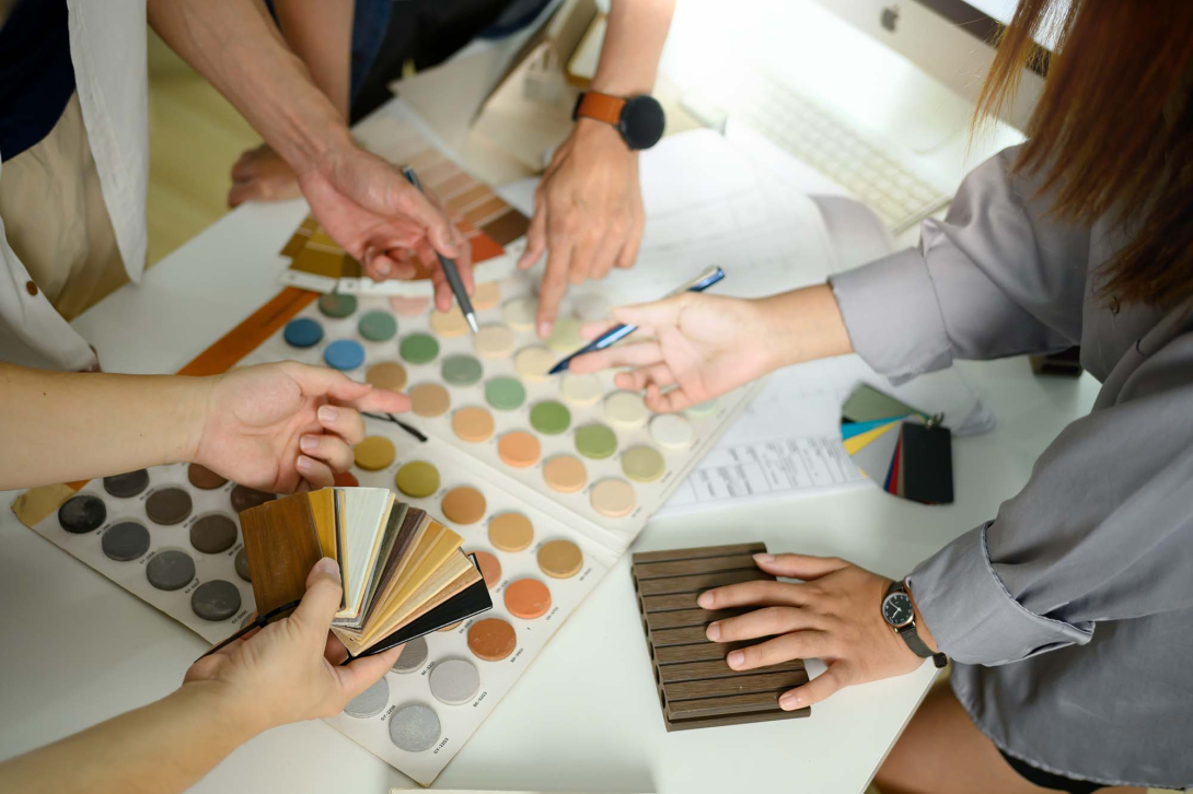Overhead view of a group collaborating around a table, comparing color swatches, material samples, and design palettes while discussing interior design options